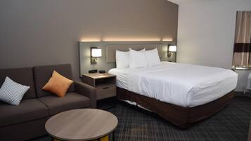 A hotel room with a bed, a sofa, a nightstand, a lamp, and a small round table.