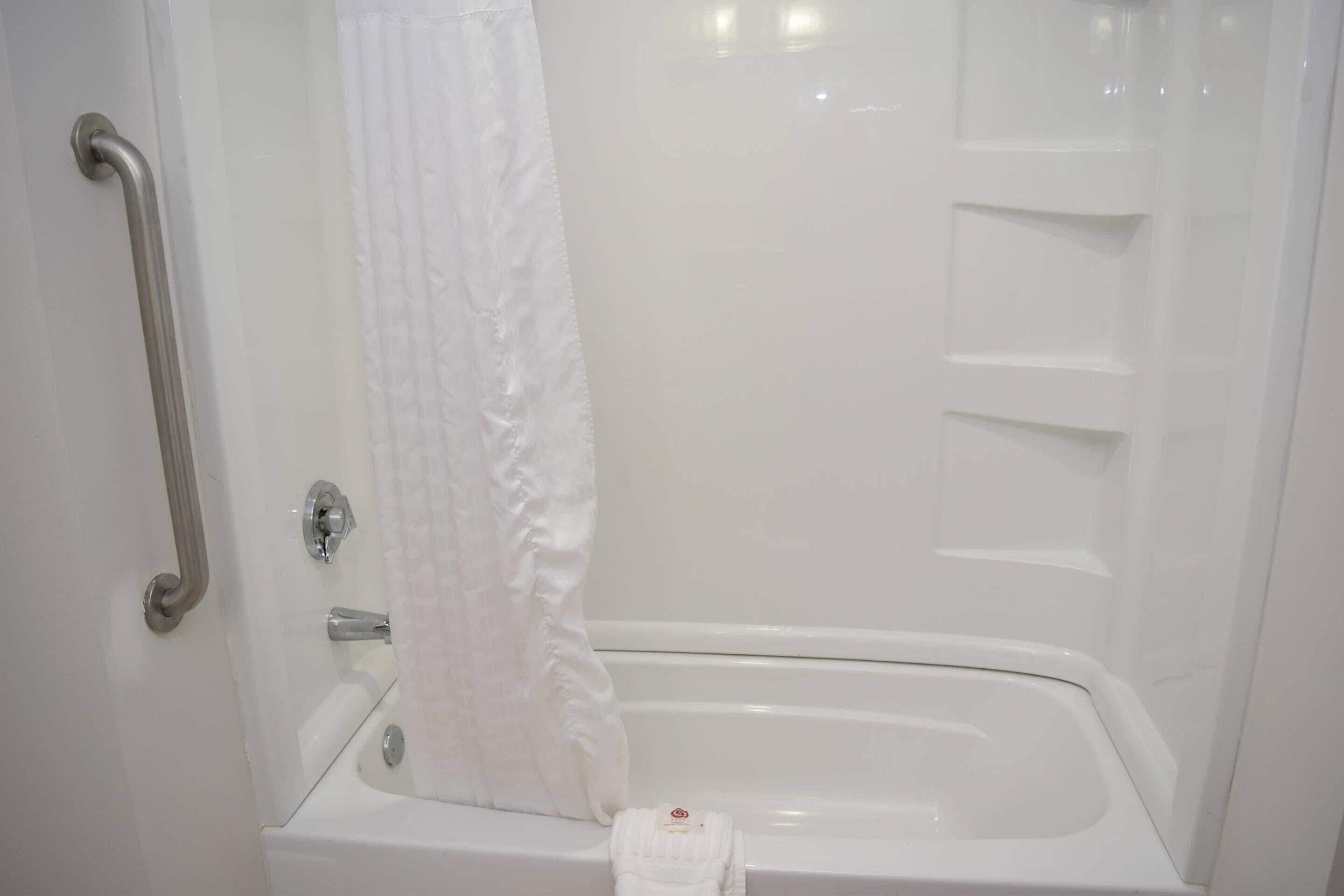 A white bathtub with a shower curtain, a grab bar, and a towel rack.