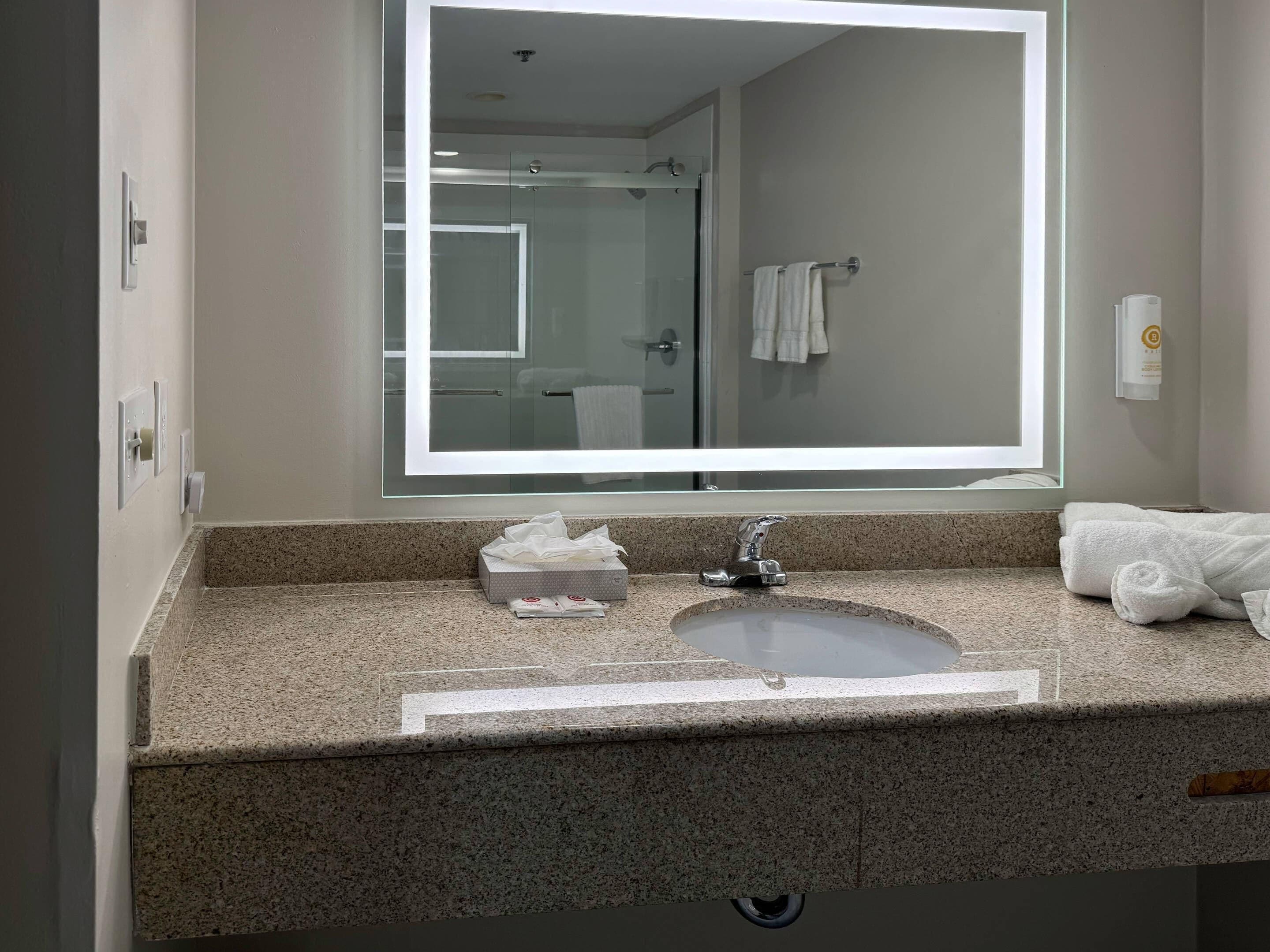 A bathroom with a granite countertop, a sink, a mirror, and a glass shower enclosure.