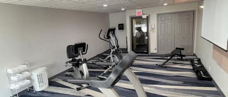 A gym with treadmills, a stationary bike, and a rowing machine. There is a white laundry basket and a white wall-mounted rack.
