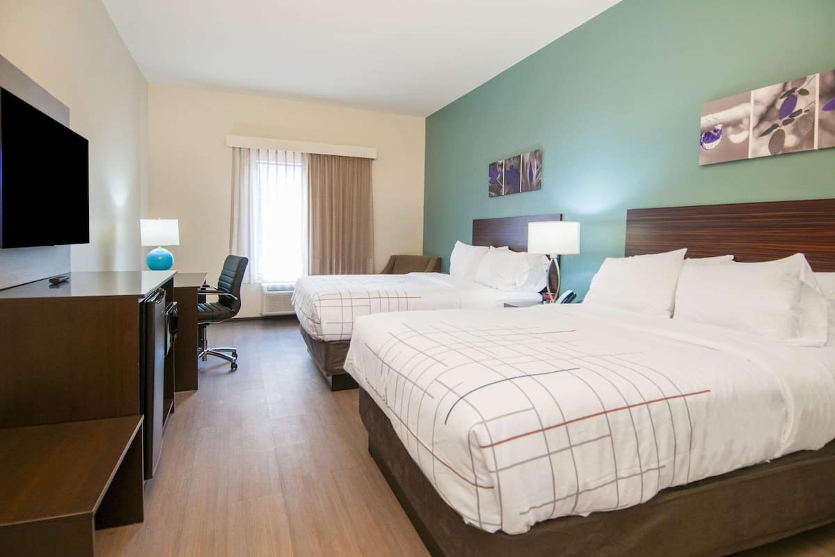 A hotel room with two beds, a desk, a chair, a TV, and a window with curtains.