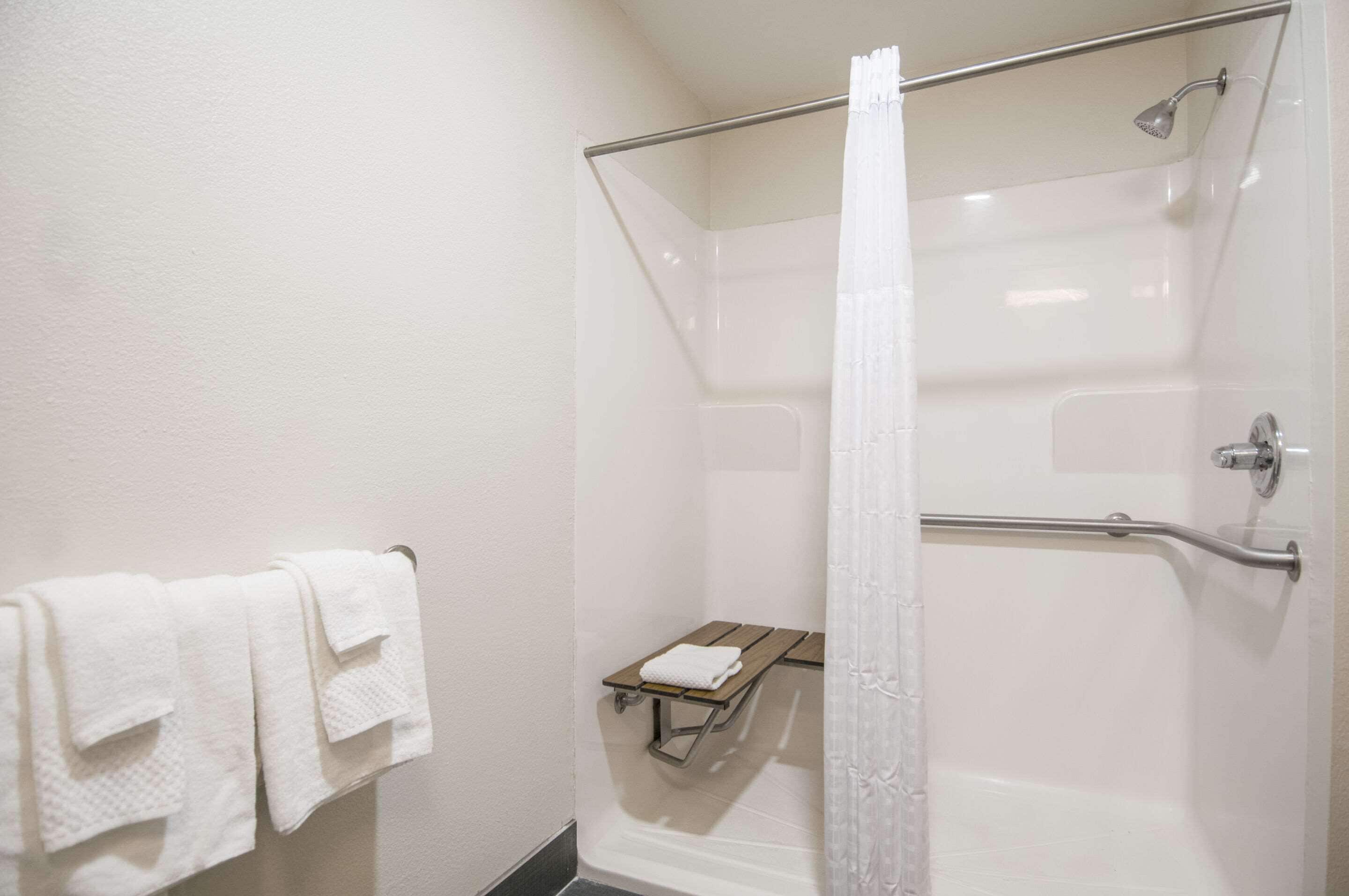 A shower with a glass door, a white towel rack, and a small wooden bench.