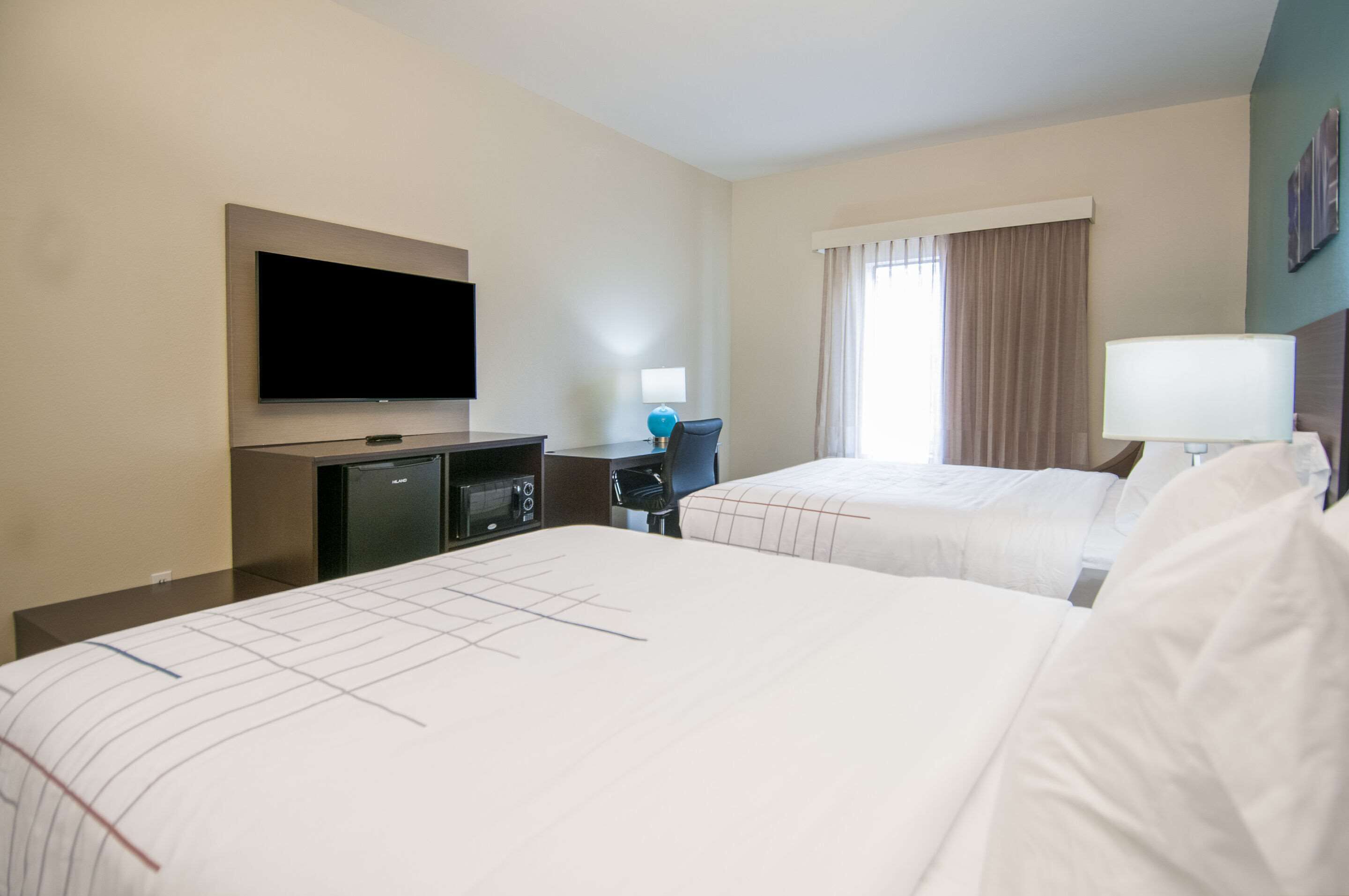 Habitación de hotel con dos camas, televisión, minibar y ventana con cortinas.