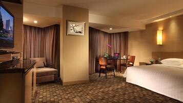 Habitación de hotel con cama, escritorio con computadora, una silla, televisor y lámpara de pared.
