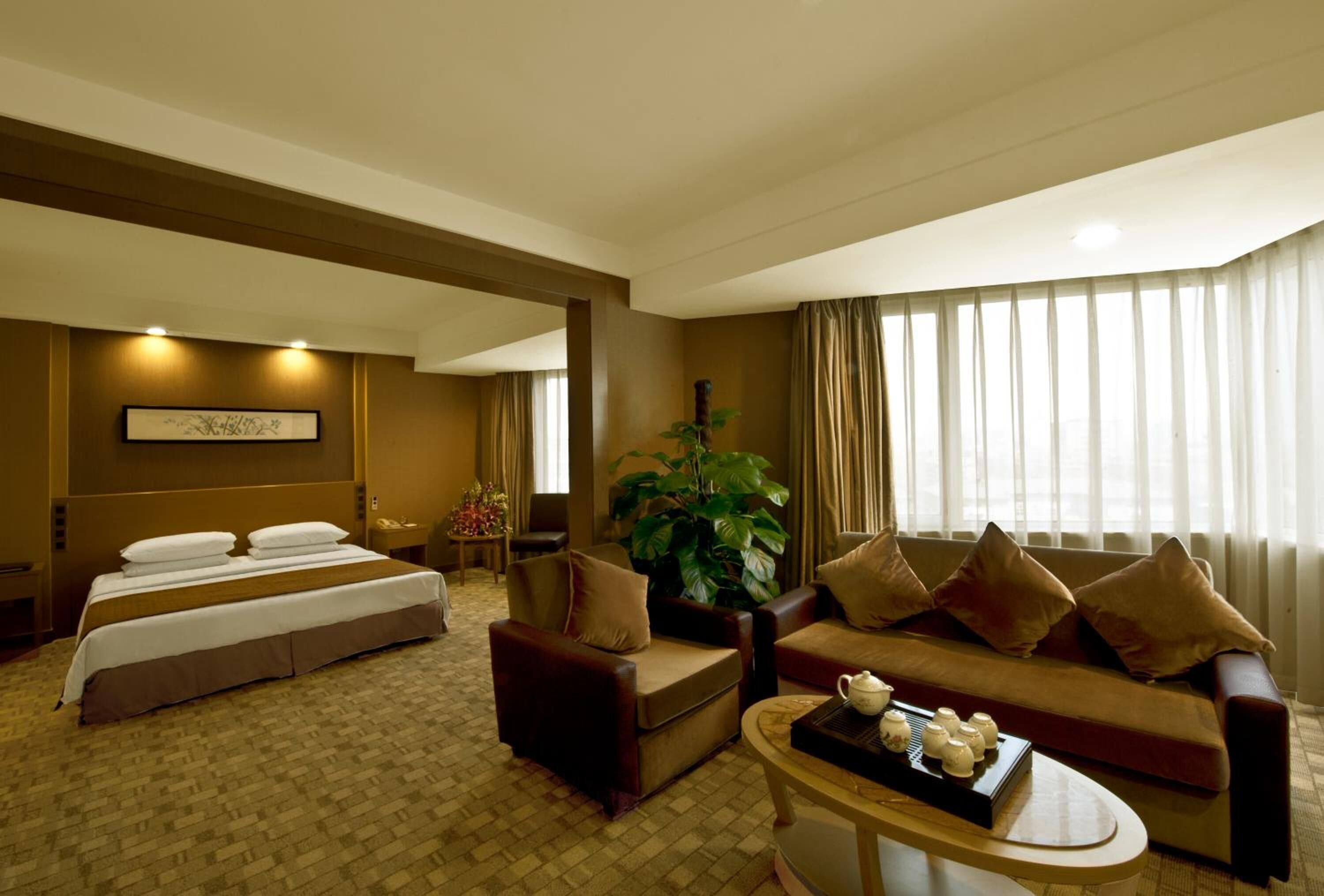 A hotel room with a large bed, two sofas, a coffee table, and a large window with curtains.