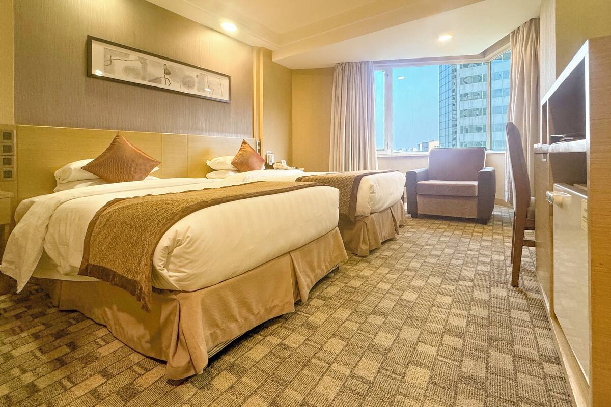 A hotel room with two beds, a sofa, a TV, and a large window with a city view.