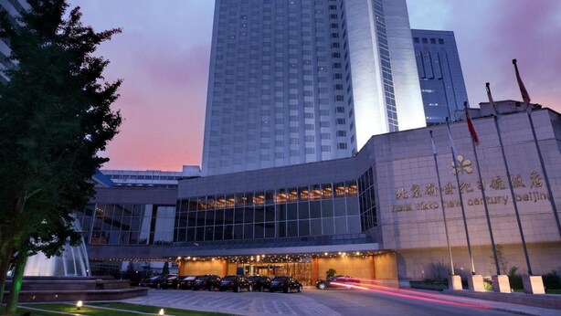 A modern hotel building with a prominent vertical sign, a well-maintained garden area, and a clear sky. - Hotel New Century Beijing (Beijing)