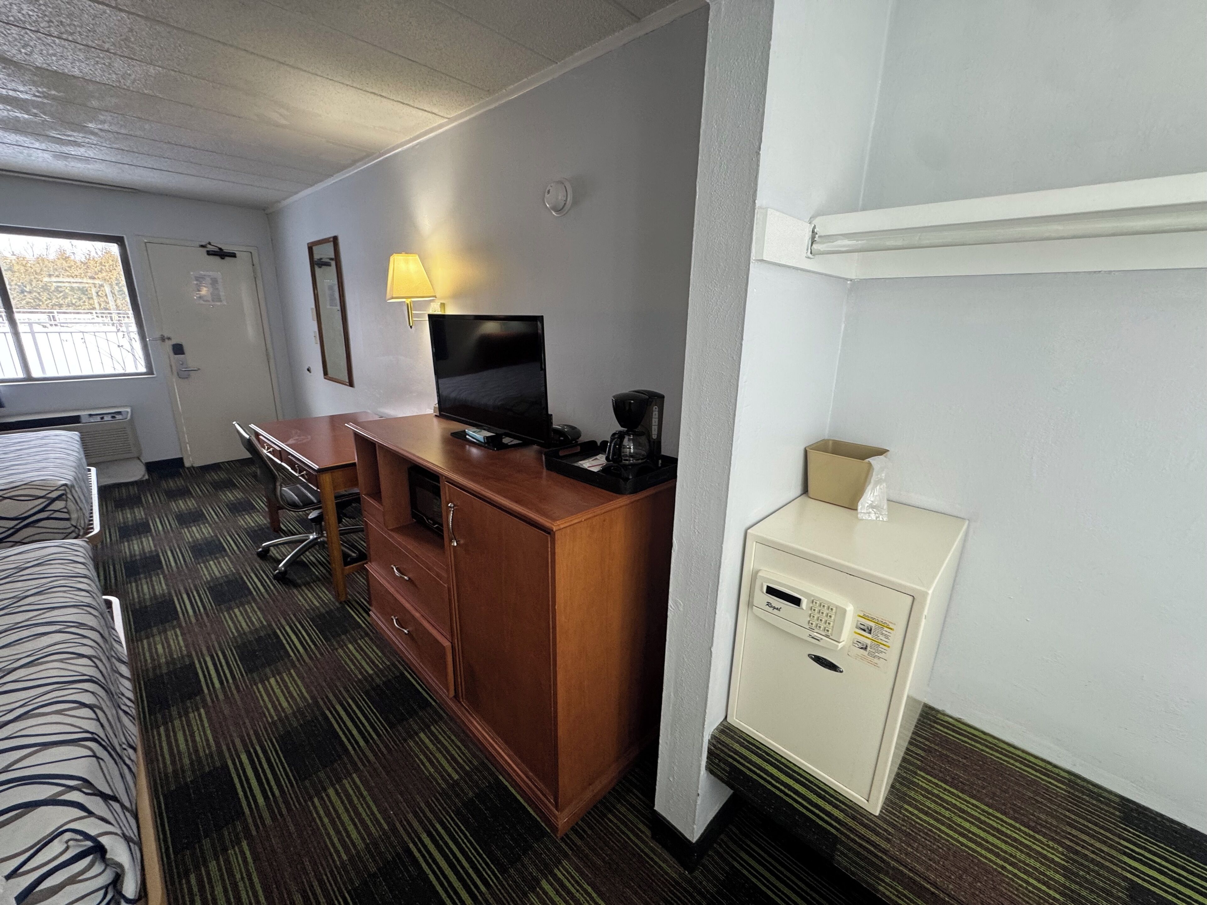 Quarto de hotel com uma cama, uma escrivaninha com computador, televisão, cafeteira e minibar.