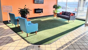 A reception area with a large TV, two blue chairs, a grey sofa, and a green carpet.