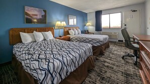 A hotel room with two beds, a desk, a chair, and a window.