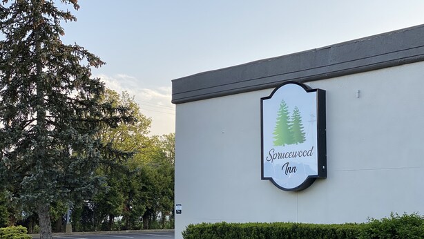 A building with a sign that reads "Sprucewood Inn" and a parking lot in the background.