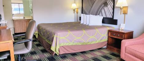 A hotel room with a bed, desk, chair, and a large window.