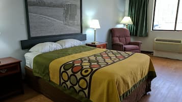 Habitación de hotel con cama, una silla, mesita de noche, lámpara y un cuadro grande en la pared.