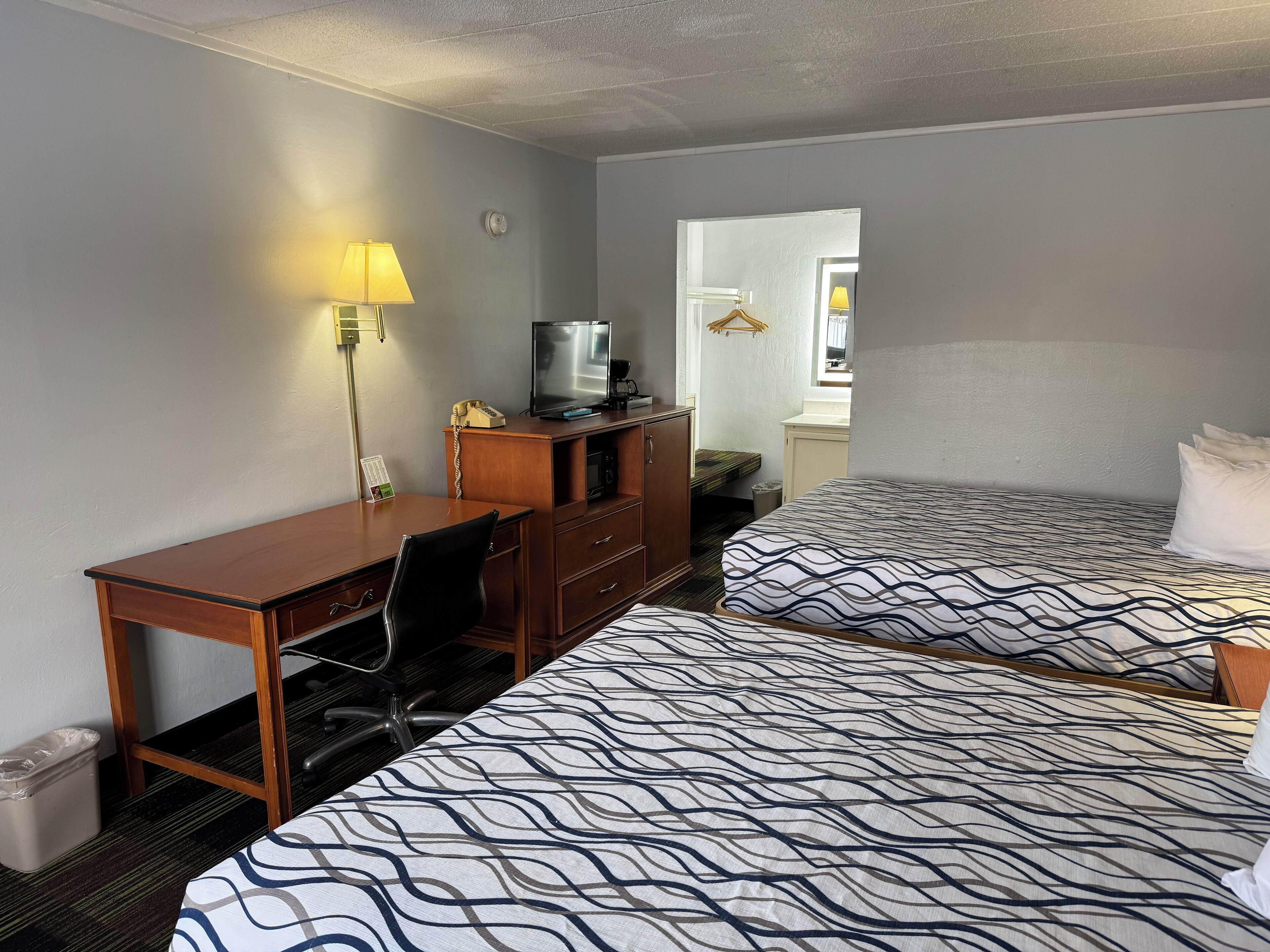 A hotel room with two beds, a desk, a chair, a telephone, a television, and a lamp.