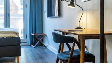 A modern room with a bed, a desk with a chair, a hanging light fixture, and a TV on the wall.