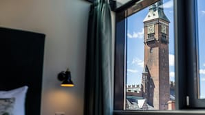 A hotel room with a large window, a bed, a nightstand, and a wall-mounted lamp. - Motel One Copenhagen (Copenhagen)