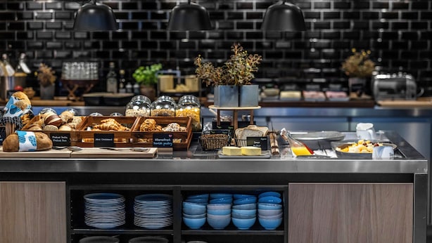 A breakfast buffet with various baked goods, a coffee station, and a selection of plates and bowls. - Motel One Copenhagen (Copenhagen)