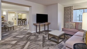 A hotel room with a flat-screen TV on a wooden stand, a sofa with patterned cushions, a dining area with a table and chairs, and a carpeted floor. - Sheraton Portland Airport Hotel (Portland)