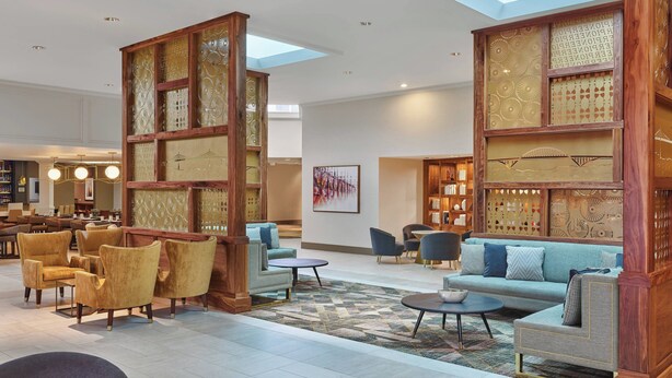 A spacious lobby with a high ceiling, a central seating area with sofas and armchairs, and a patterned wooden partition. - Sheraton Portland Airport Hotel (Portland)