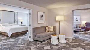A hotel room with a bed, a sofa, a lamp, and a small table. - Sheraton Portland Airport Hotel (Portland)