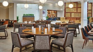 A spacious dining area with round tables and modern chairs, featuring geometric pendant lighting and a large bookshelf in the background. - Sheraton Portland Airport Hotel (Portland)