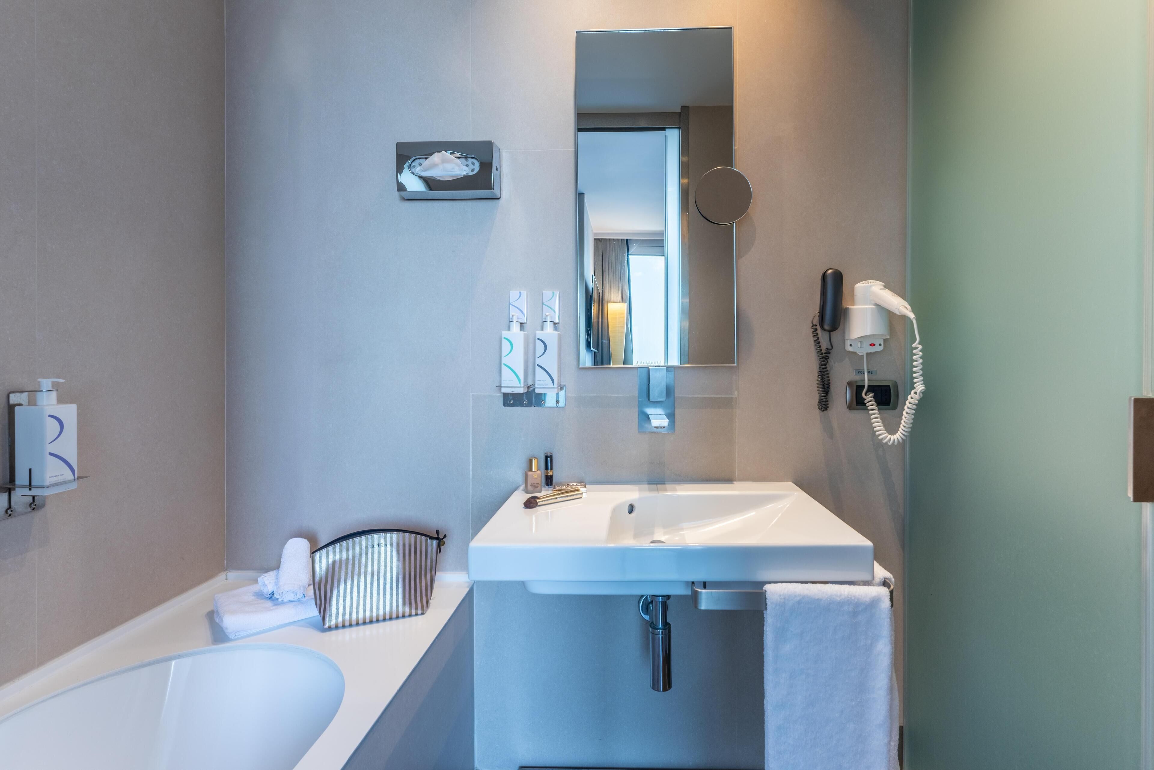 Ein modernes Badezimmer mit einem weißen Waschbecken, einem Spiegel, einem Handydurchgang und einer Badewanne.