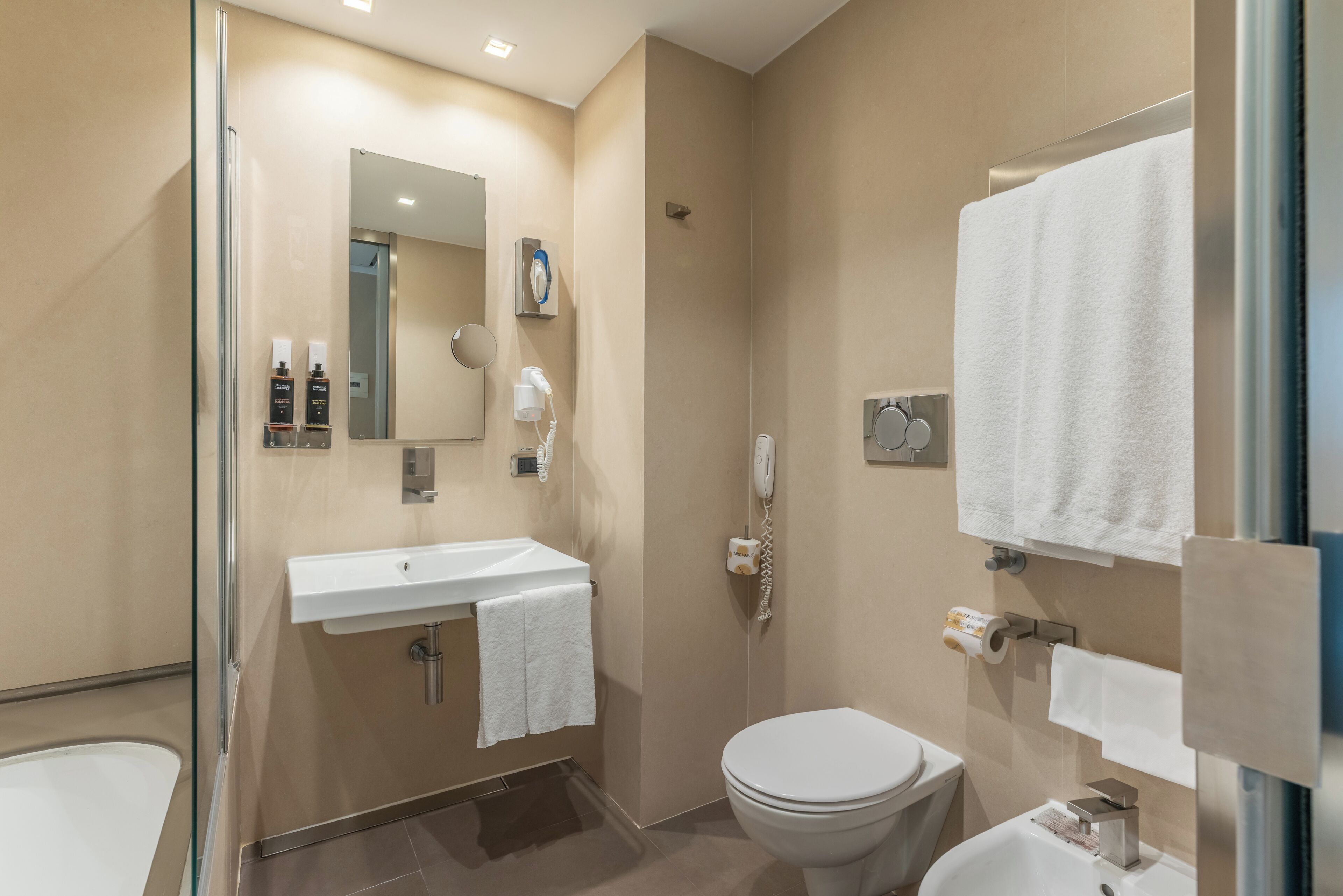 A modern bathroom with a glass shower enclosure, a white sink, a toilet, and a mirror.