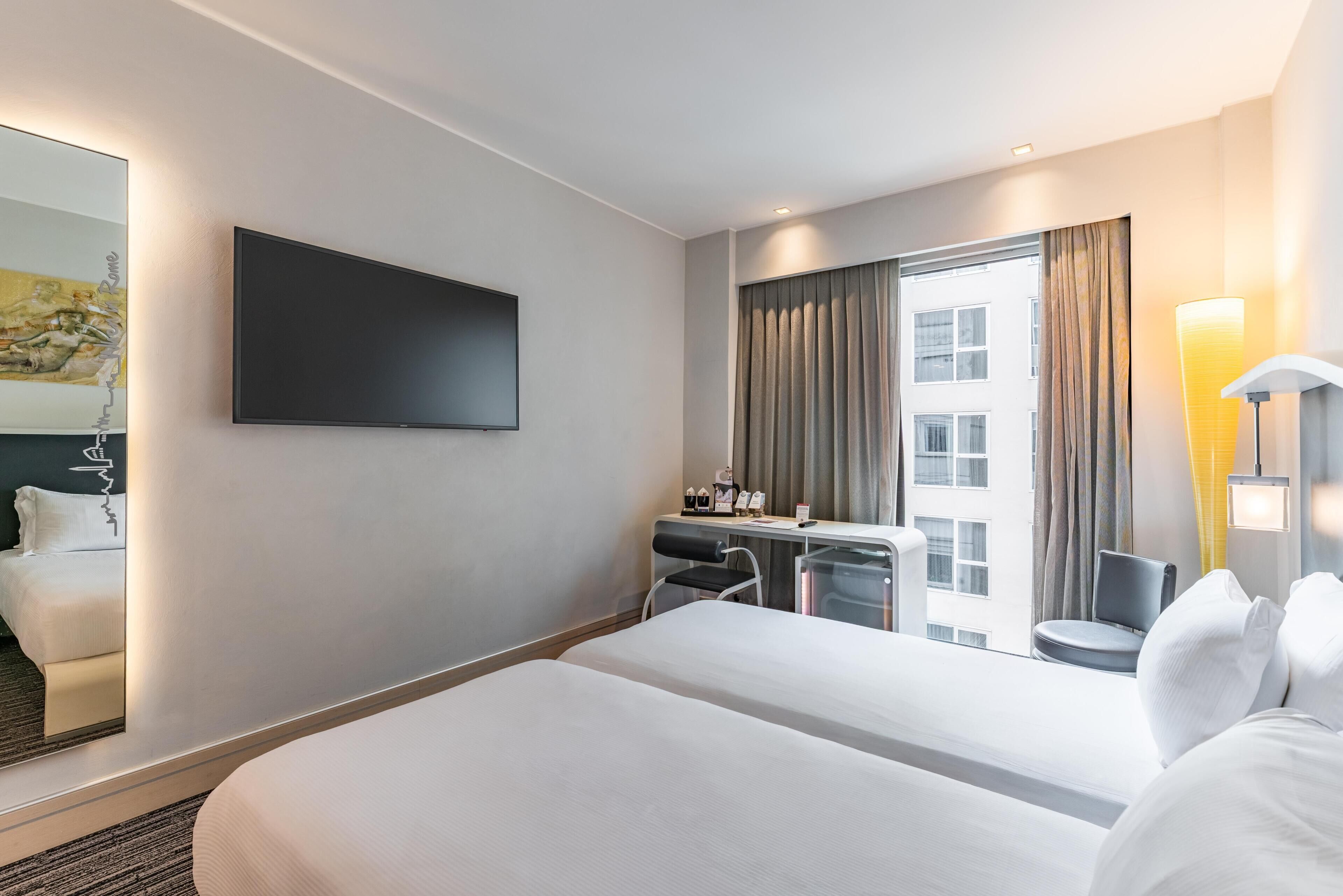 A hotel room with a bed, a desk, a chair, a TV, and a window with curtains.