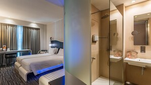 Une chambre d’hôtel équipée d’un lit, d’un bureau et d’une douche séparée par des parois en verre.