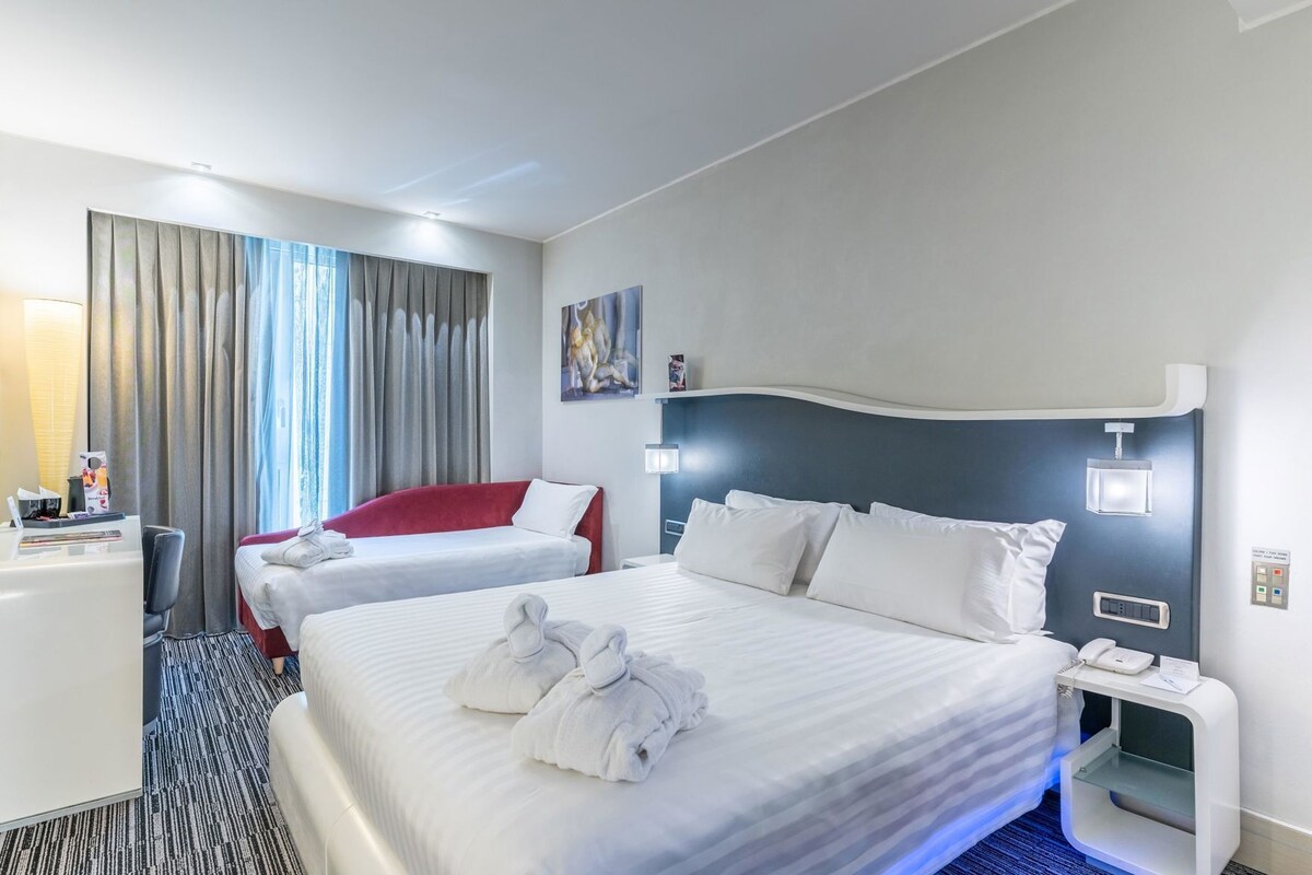 Une chambre d’hôtel avec deux lits, un bureau, une chaise, une table de chevet et un tableau au mur.