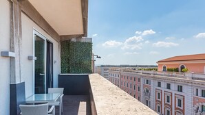 Un balcon avec une table et des chaises en verre, un mur végétal et une vue sur les immeubles.