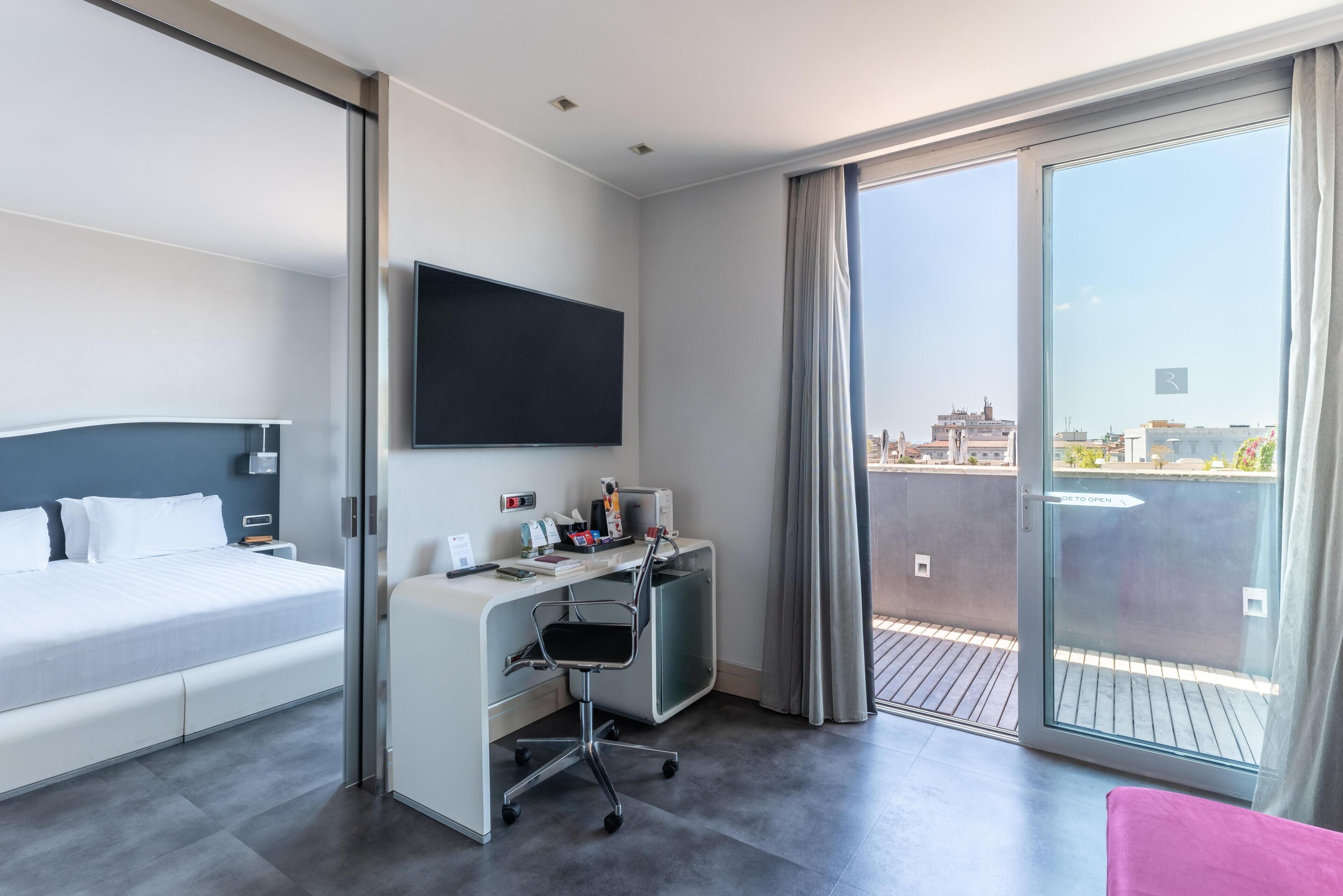 Habitación de hotel con cama, escritorio, silla y televisor.