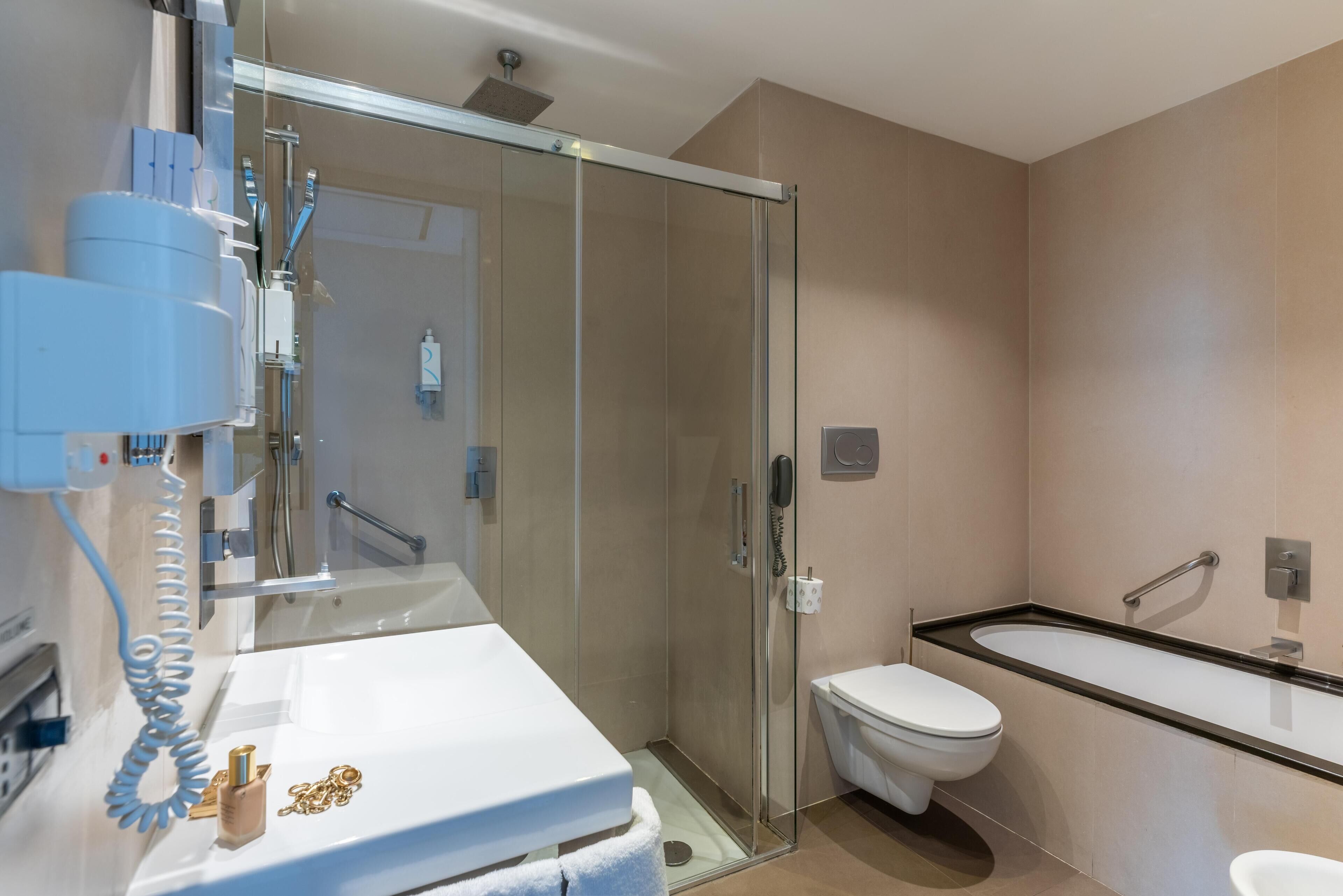 Een moderne badkamer met een douchecabine van glas, een wit wastafelmeubel met gouden details, een toilet en een bad.
