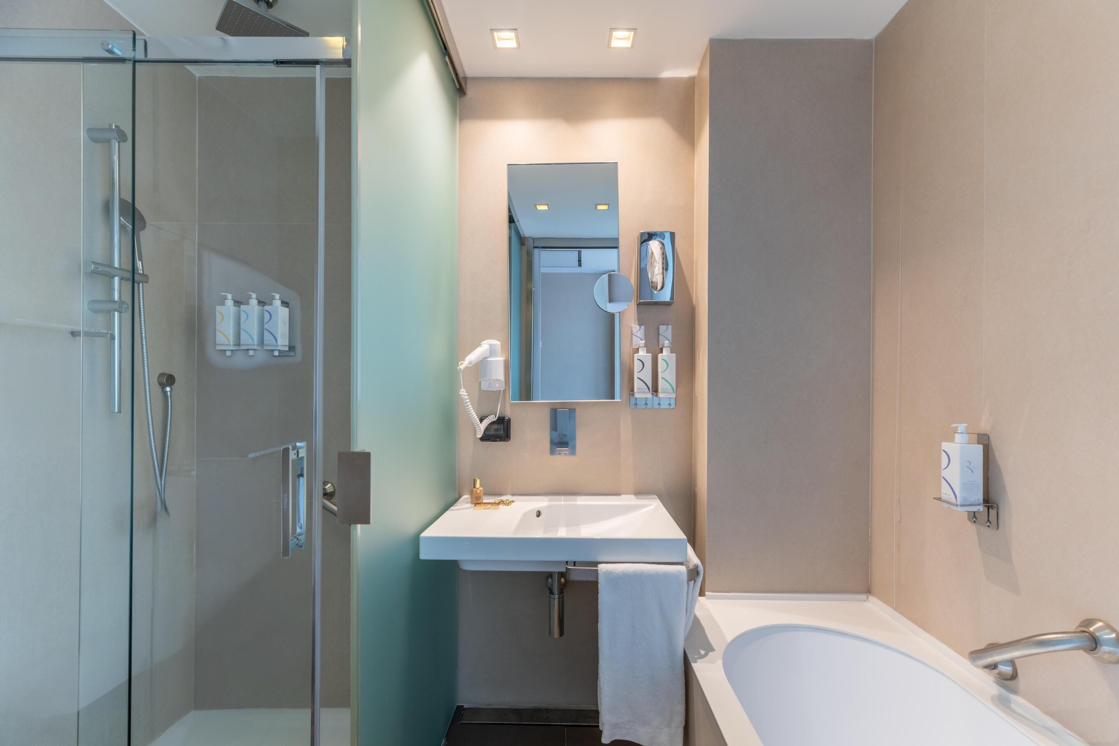 A modern bathroom with a glass shower enclosure, a white sink, a mirror, and a bathtub.