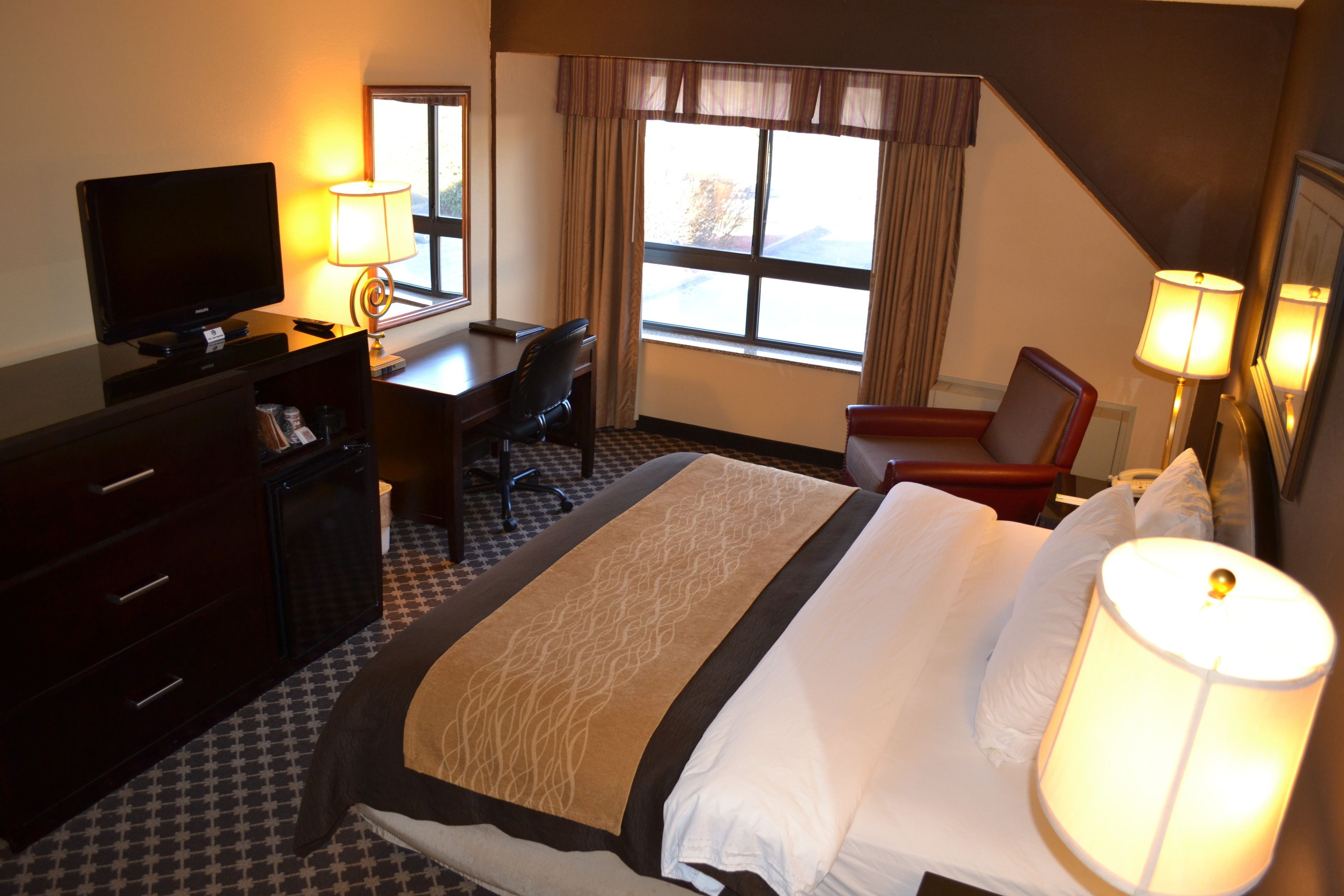 A hotel room with a large bed, a desk with a chair, a television, and two lamps.