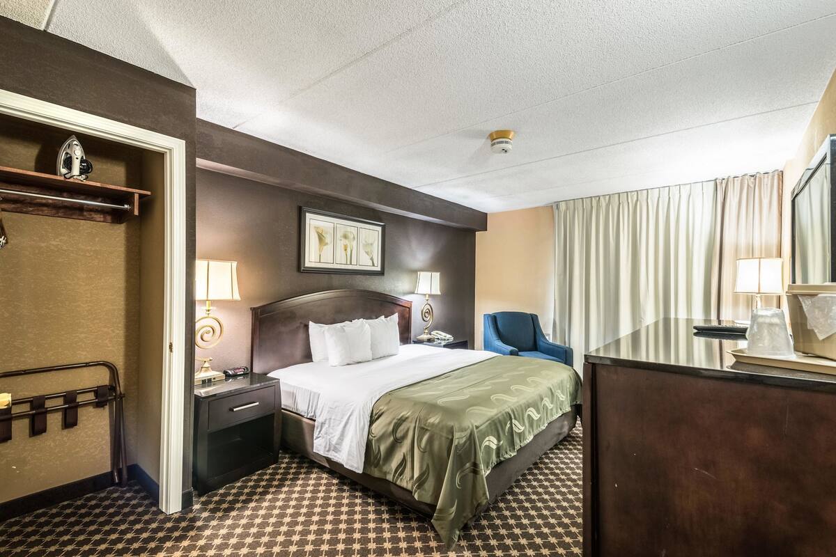 Une chambre d’hôtel comprenant un lit, des tables de chevet, une chaise, un bureau et un grand miroir.
