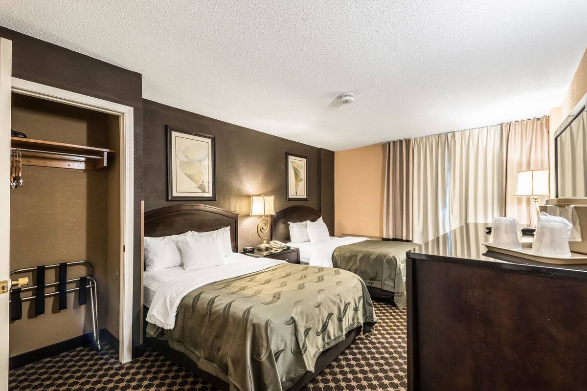 Une chambre d’hôtel avec deux lits, un bureau, un miroir et une fenêtre avec des rideaux.