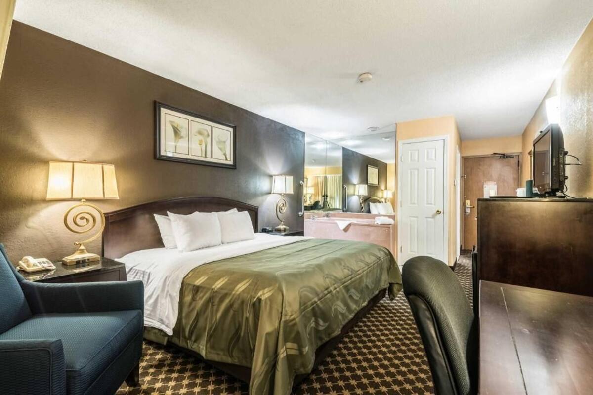Une chambre d’hôtel avec un lit, un bureau, une chaise, une télévision et une salle de bain visible au fond.
