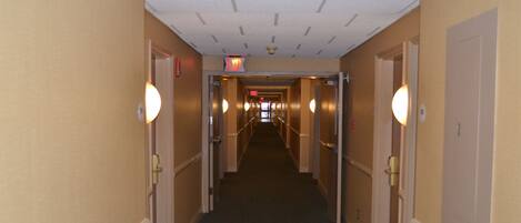 A hotel hallway with a carpeted floor, doors on both sides, and a ceiling with recessed lighting.