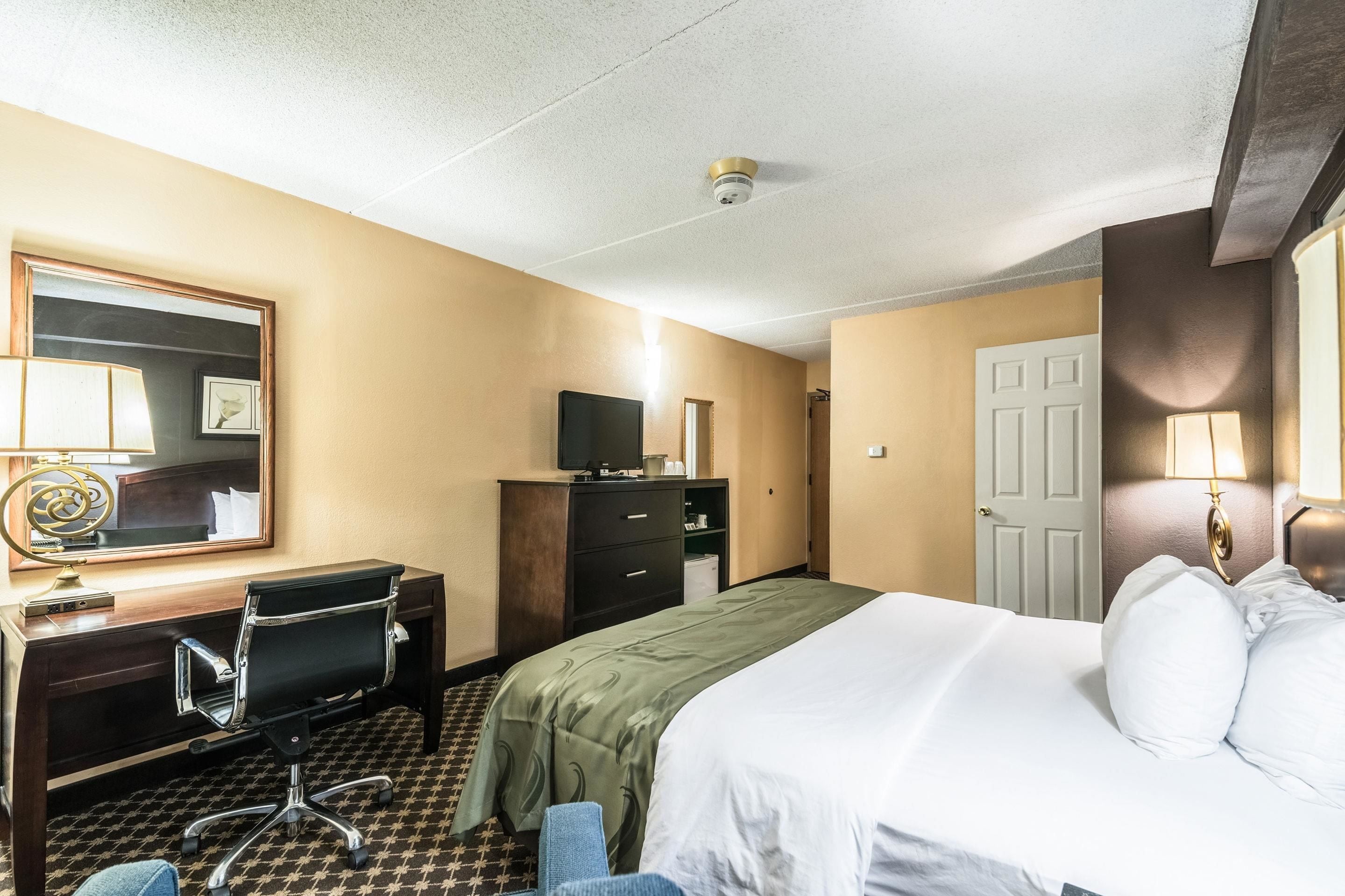 A hotel room with a bed, desk, chair, dresser, and a television.