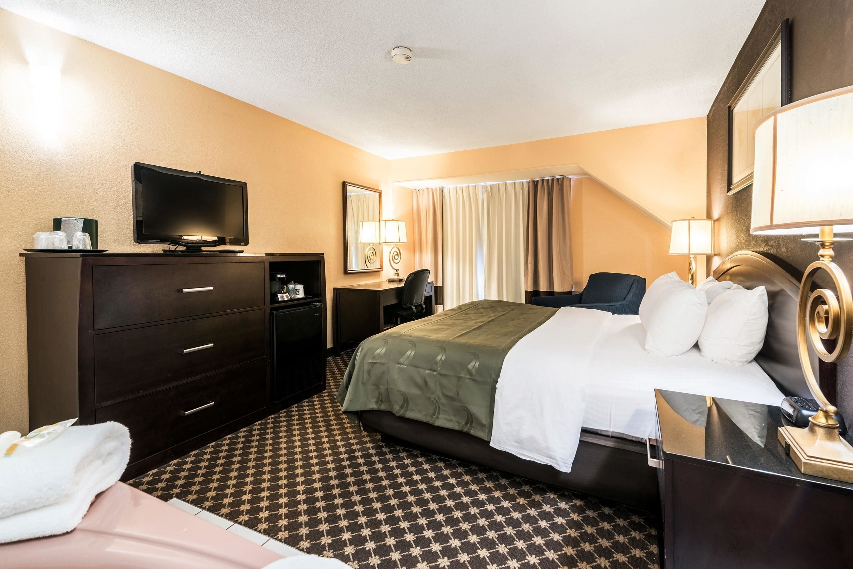 Une chambre d’hôtel équipée d’un lit, d’une télévision, d’un bureau avec une lampe, d’une chaise et d’une commode.