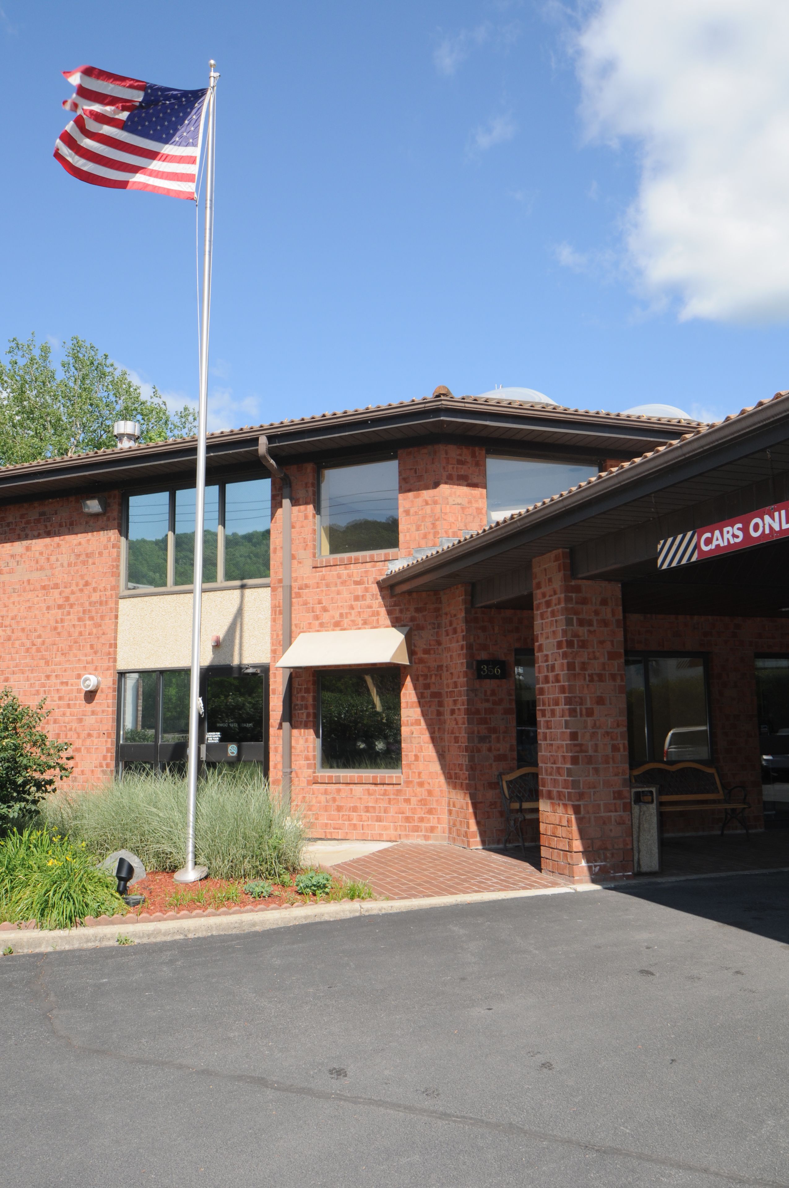 A brick building with a flagpole, a sign reading "CARS ONLY", and a parking lot.
