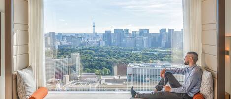 A man sitting on a sofa by a large window with a cityscape view.