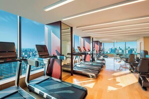 A gym with treadmills, exercise bikes, and a city view.