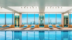 A modern indoor pool with clear blue water, large windows offering a city skyline view, and sun loungers along the poolside. - The Prince Gallery Tokyo Kioicho, a Luxury Collection Hotel (Tokyo)