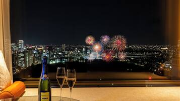 A bottle of champagne and two glasses on a table with a cityscape and fireworks in the background.