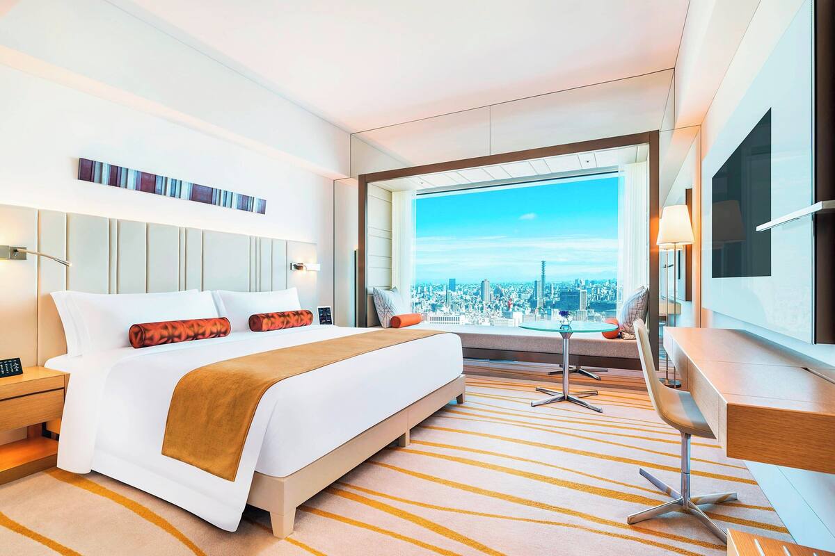 A modern hotel room with a large bed, a desk, and a view of a cityscape.