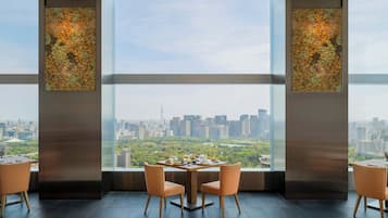 A dining area with a table set for two, large windows offering a city view.