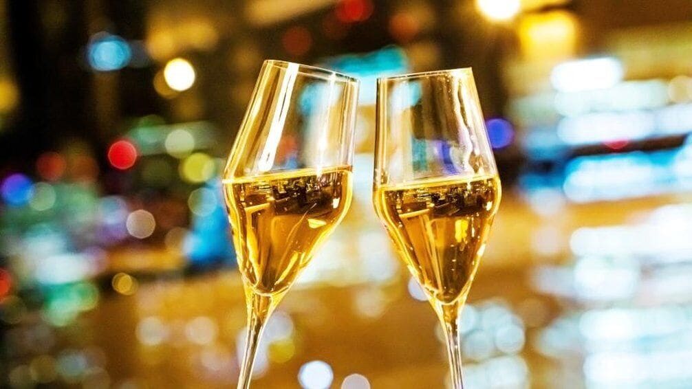 Two champagne flutes with a blurred background of lights.