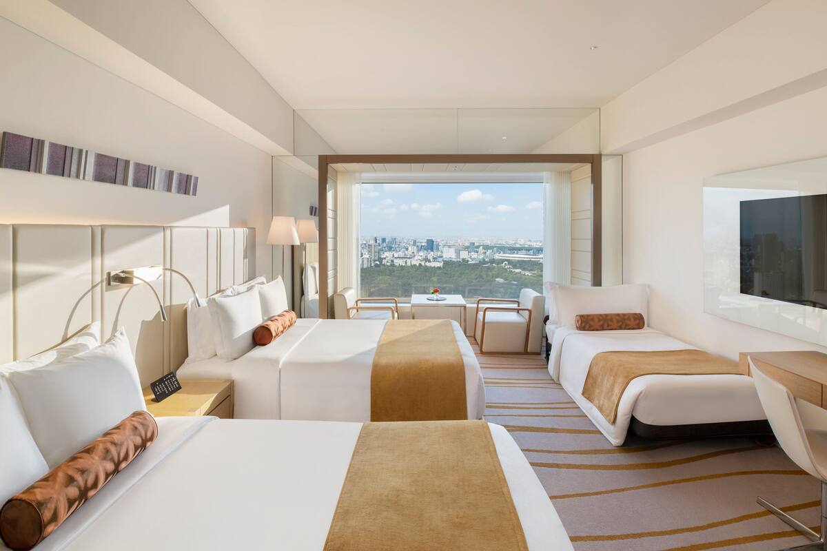 A hotel room with two beds, a desk, a chair, and a large window with a city view.